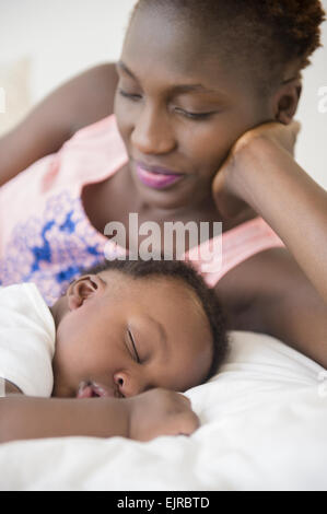 Black mother admiring sleeping son on bed Stock Photo