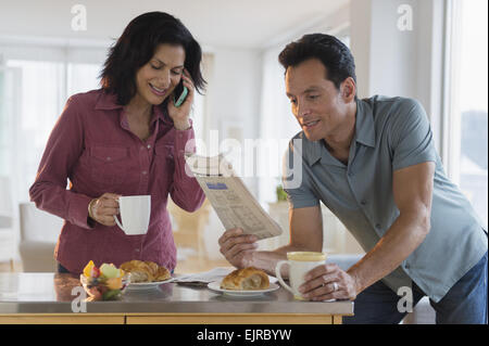 Couple reading newspaper and talking on cell phone at breakfast Stock Photo