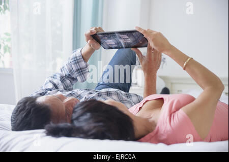 Couple using digital tablet and laying on bed Stock Photo