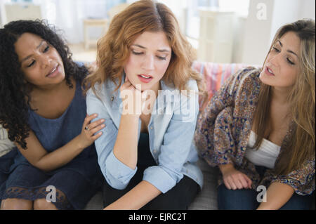 Women comforting sad friend on sofa in living room