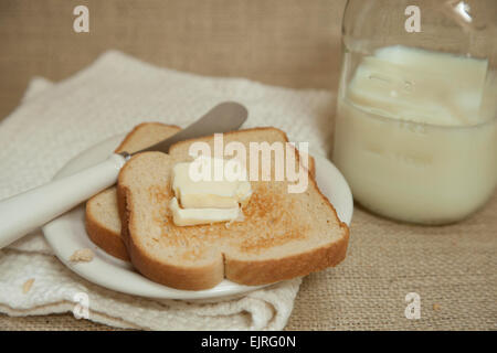 Two slices of toast rest on a cream colored plate; butter knife placed to the side of toast Stock Photo