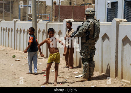 A young Iraqi boy strikes a muscle pose while standing next to a passing U.S. Soldier from Charlie Company, 1st Battalion, 35th Armor Regiment as he provides security outside a recreation center during a patrol in the in the Thawra 1 neighborhood of the Sadr City district of Baghdad, Iraq, June 6, 2008.  Tech Sgt. Cohen A. Young Stock Photo