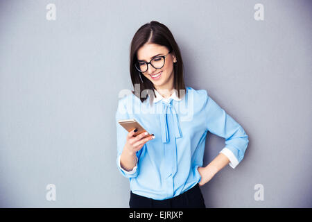 Smiling businesswoman using smartphone over gray background. Wearing in blue shirt and glasses. Stock Photo