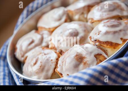 Cinnamon buns sit on a blue and white checked towel, straight from the oven. An icing glaze tops them. Stock Photo