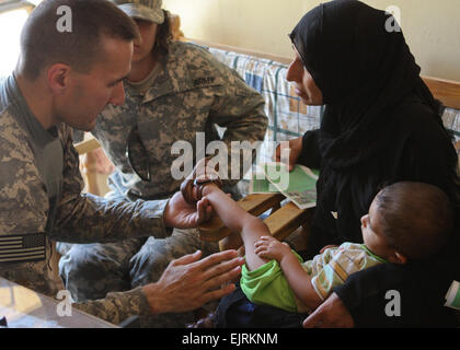 Maj. Kurt Kinney, a native of Utica, N.Y., who serves as battalion surgeon with 1st Battalion, 21st Infantry Regiment, 2nd Stryker Brigade Combat Team, 25th Infantry Division, Multi-National Division – Baghdad, looks at a rash on young boy’s leg while the boy’s mother holds him during a cooperative medical engagement in Sheik Lateef Village west of Baghdad, Aug. 12, 2008. Stock Photo