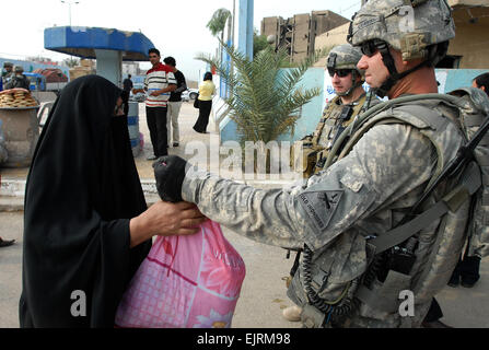 Staff Sgt. Derek Detherow, a native of Wasilla, AK, 2nd Platoon, C Co. 135th Armor currently attached to Task Force 1/6, hands a food parcel to a woman in the Sadr City district of Baghdad, Oct. 23 as 1st Lt. Christopher Yong, a native of Whittier, Calif., and Staff Sgt. Detherow's platoon leader watches. Each parcel contained 1 liter of water, a can of meat, a bag of beans, a bag of rice, a package of tea, two packages of pasta, a can of peas and a can of tomatoes. The food was requested by a member of the Sadr City District Advisory Council.  Sgt. Jerry Saslav, 3rd BCT PAO, 4th Inf. Div. Stock Photo