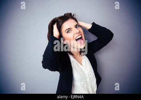 Young businesswoman shouting over gray background. Holding her hair. Looking at camera Stock Photo