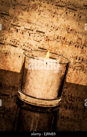 Old classical sheet music has a vintage tone and texture to it; vertical format; candle burning in foreground Stock Photo