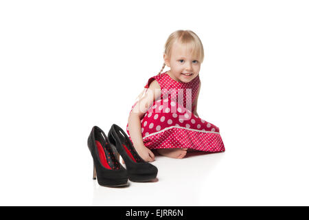 Smiling little girl sitting near big shoes. Isolated on white background Stock Photo