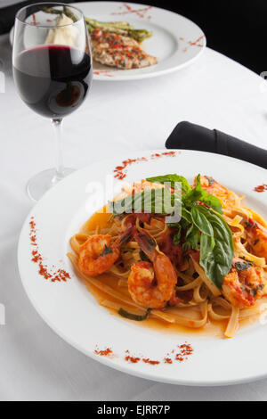 A white plate holds linguine with shrimp in a fra diavolo sauce, topped with fresh basil. Paprika is sprinkled on the plate. Stock Photo