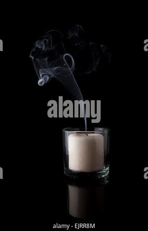 Smoke rises from a white candle that has just been blown out; black reflective background Stock Photo