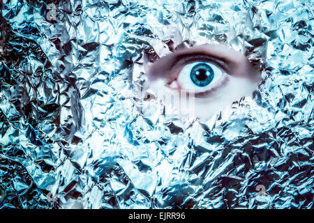 An eye peeks out of  a mask of tin foil.  Looks frightening and surreal.  Split color tone Stock Photo