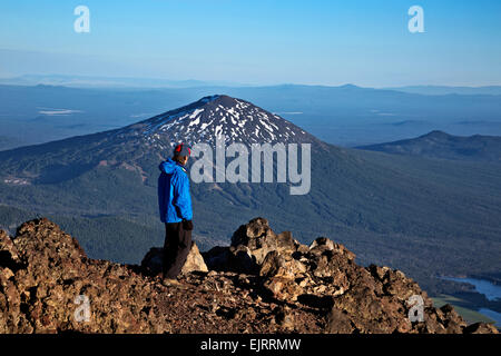 OREGON - Hiker overlooking Mount Bachelor and Sparks Lake from crater rim at summit of South Sister in Three Sisters Wilderness. Stock Photo