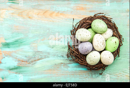 Pastel colored easter eggs in nest on wooden background. Festive decoration Stock Photo