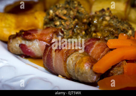 Uneaten Christmas dinner including pigs in blankets, stuffing, parsnip, carrots and roast potatoes in gravy on a white plate. Stock Photo