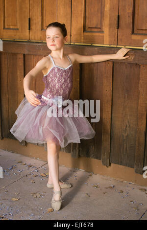 A young ballerina poses against a wood paneled wall. Stock Photo