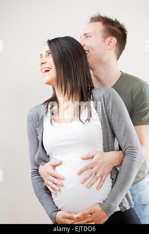 happy couple with pregnant woman. the woman smiles while his husband holds her in his arms touching her belly in which they wait Stock Photo