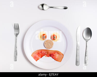 sad emoticon food, made from cheese, tomatoes, bread and ham on a plate with cutlery Stock Photo