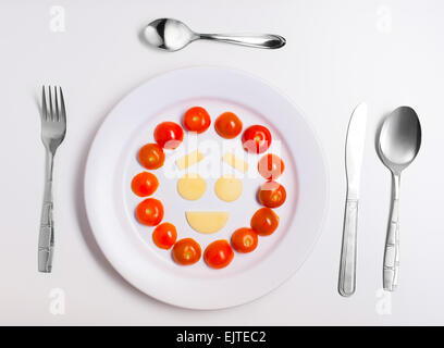 laughing emoticon food, made from cheese and tomatoes, on a plate with cutlery, isolated Stock Photo