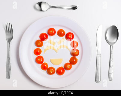 laughing emoticon food, made from cheese and tomatoes, on a plate with cutlery, isolated Stock Photo