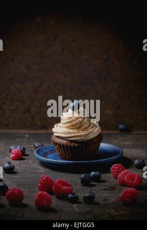 Chocolate cupcake with butter coffee cream and fresh berries over dark background Stock Photo