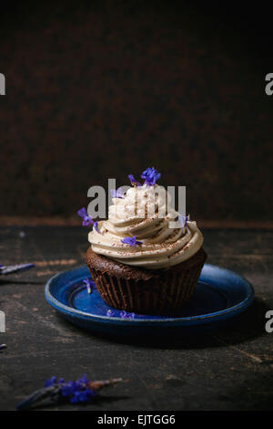 Blue plate with chocolate muffin with coffee butter cream and edible lavender flowers over dark surface Stock Photo