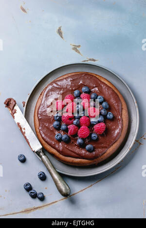Chocolate cake with fresh berries and chocolate cream, served with vintage knife over gray metal background. Top view Stock Photo