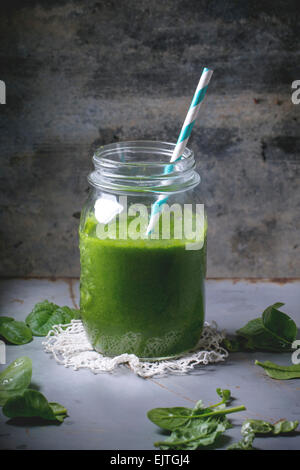 Glass jar with green smoothie, served with baby spinach leaves over metal table Stock Photo