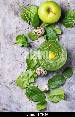 Glass of green smoothie with quail egg's yolk, green apple and baby spinach leaves over tin surface. Top view. Stock Photo