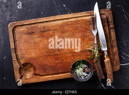 Chopping cutting board, seasonings and rosemary with fork and knife carving set on dark marble background Stock Photo