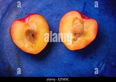 Nectarine halves in the shape of heart over blue ceramic background. Top view. Stock Photo