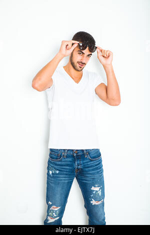 casual young handsome man in white shirt next to a wall, wearing sunglasses Stock Photo