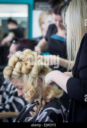 Hairdressers styling two female models in a hair salon for a fashion show,with the one in the foreground having curly blond hair Stock Photo