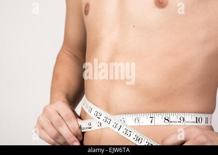 White teenage boy measuring his stomach. Studio shot Stock Photo