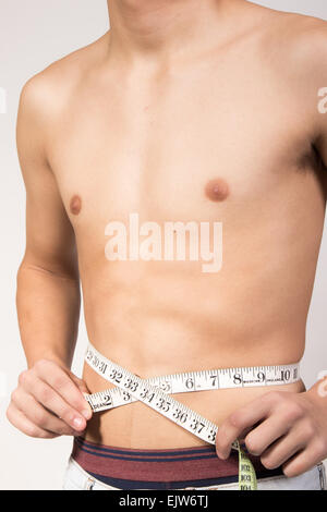 White teenage boy measuring his stomach. Studio shot Stock Photo
