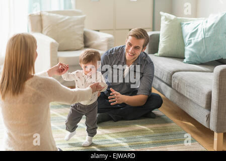Happy parents helping little son (2-3 years) walking in living room Stock Photo