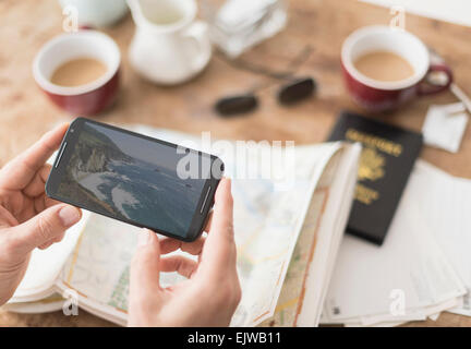 Close up of man's hand holding smartphone above map Stock Photo