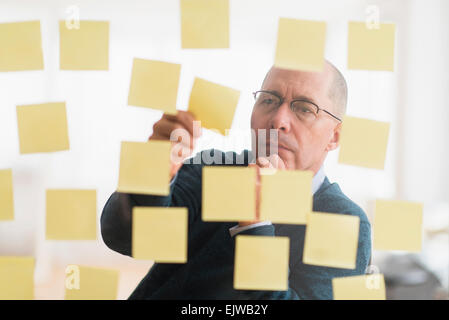 Businessman arranging adhesive notes on glass wall Stock Photo