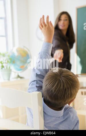 Female teacher standing beside blackboard in classroom, schoolboy (6-7) with hand raised Stock Photo