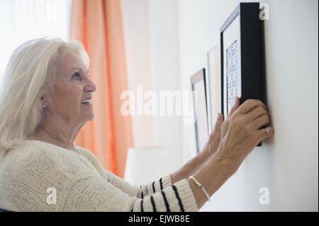 Senior woman hanging picture frame on wall Stock Photo