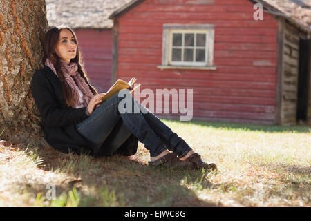 USA, Montana, Whitefish, Woman with book sitting under tree Stock Photo