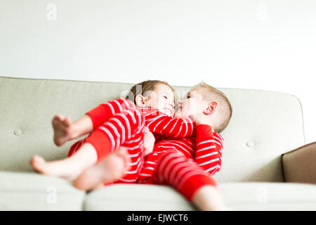 Siblings (2-3, 4-5) in red pajamas playing on sofa Stock Photo