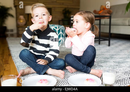 Brother (6-7) and sister (4-5) eating cookies in living room Stock Photo