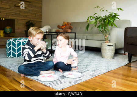 Brother (6-7) and sister (4-5) drinking milk on living room floor Stock Photo