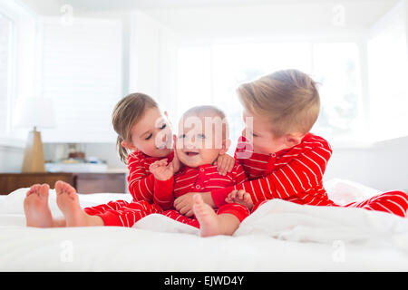 Boy (6-7) and girl (4-5) embracing brother (2-3) on bed Stock Photo