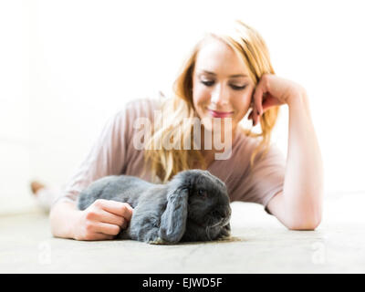 Young woman lying on floor and stroking rabbit Stock Photo