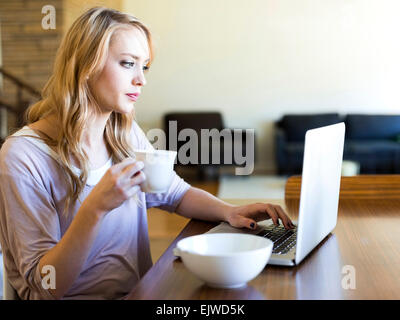 Young woman using laptop and drinking coffee at table Stock Photo