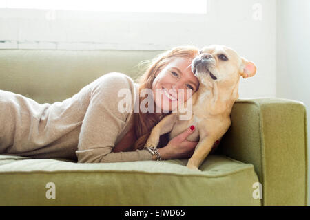 Woman lying on sofa embracing pug Stock Photo