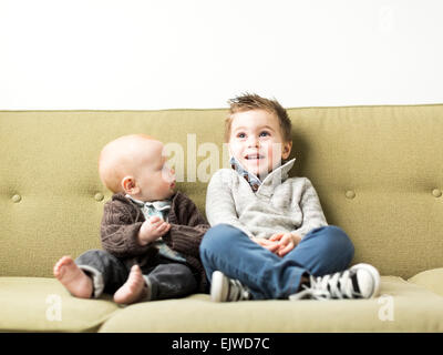 Baby boy (2-3) and brother (6-11 months) sitting on sofa Stock Photo