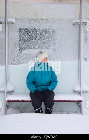 USA, Massachusetts, Boston, Middle aged woman sitting in bus stop, winter snow Stock Photo